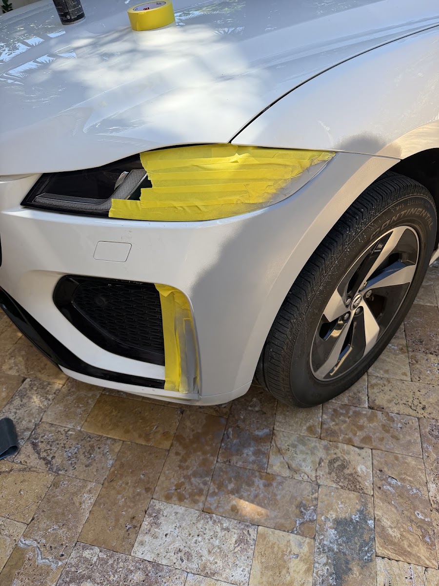 White car bumper masked and prepped for scratch repair on a driveway