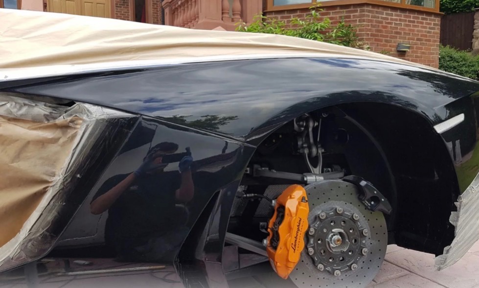 Luxury car with wheel removed and masked bodywork in progress
